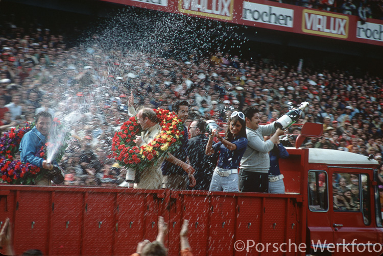 A jubilant Hans Herrmann and Richard Attwood are given a ride on the back of a truck as they celebrate Porsche’s first victory