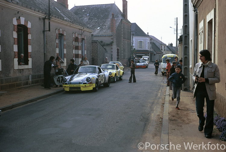 Parked in the street outside the Teloché workshop prior to setting off for the circuit is the #47 and #48 Porsche 911 Carrera RSR